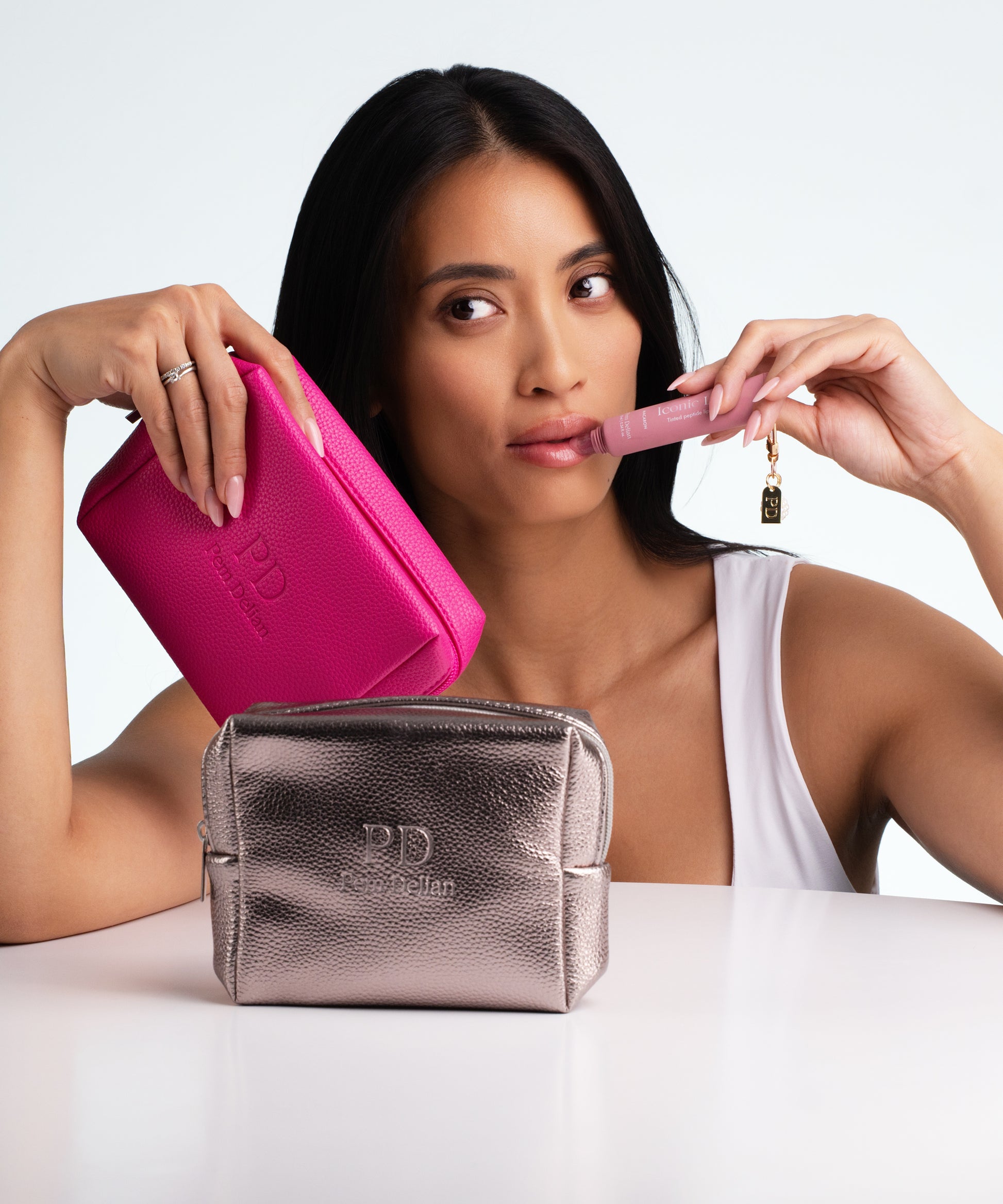 Pem Delian ezüst és pink sminktáska az asztalon, Iconic Lips Macaron a modell kezében használat közben