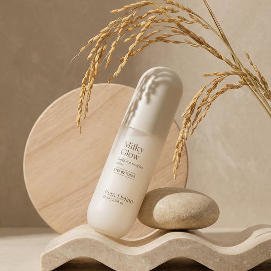 Pem Delian Milky Glow toner egy kőnek támasztva áll fa dísz előtt és búzakalász lóg be a sarokból fölé