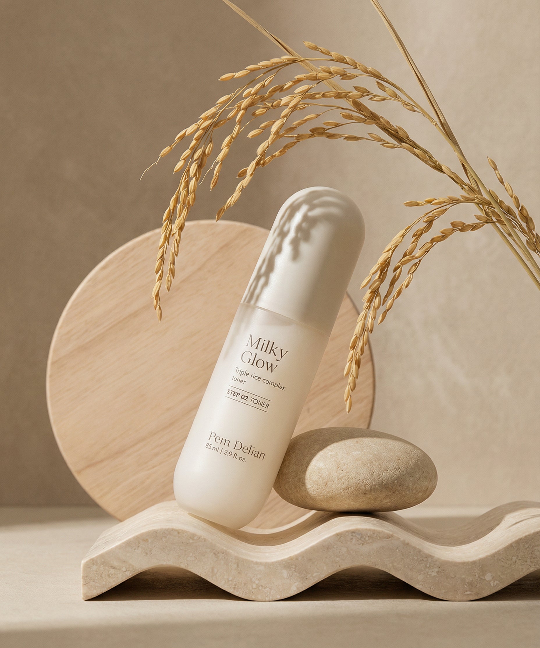 Pem Delian Milky Glow toner egy kőnek támasztva áll fa dísz előtt és búzakalász lóg be a sarokból fölé