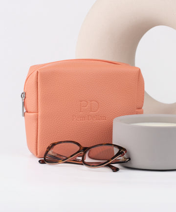 Pem Delian barack színű vegán bőr sminktáska mögött vza, előtte szemüveg és gyertya