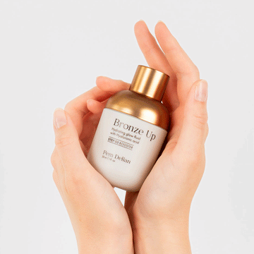 Pem Delian Bronze Up hidratáló, ragyogásfokozó fluid hialuronsavval tégelye kézben tartva