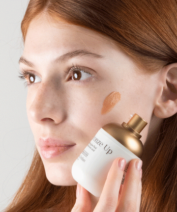 Pem Delian Bronze Up hidratáló, ragyogásfokozó fluid hialuronsavval vörös hajú modell kezében, textúra az arcon