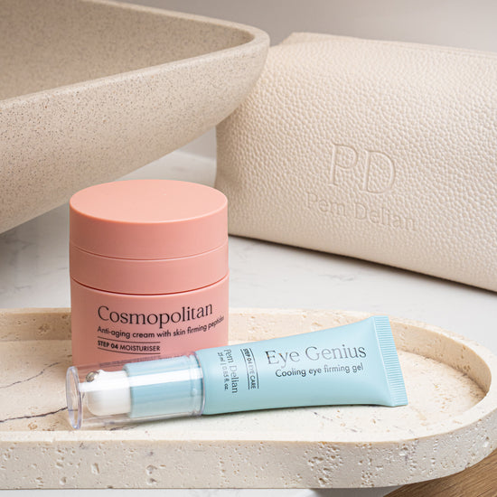 Pem Delian Cosmopolitan arckrém feszesítő peptidekkel fürdőszobában egy kő tálcán, mellette egy bézs neszesszer és Eye Genius szemkörnyékápoló