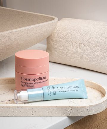 Pem Delian Cosmopolitan arckrém feszesítő peptidekkel fürdőszobában egy kő tálcán, mellette egy bézs neszesszer és Eye Genius szemkörnyékápoló