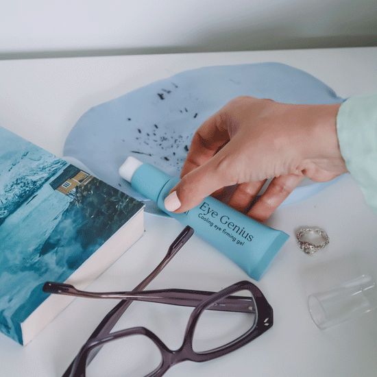 Pem Delian Eye Genius hűsítő szemkörnyékfeszesítő gél kupak nélkül kézben, szemüveg, könyv, gyűrű mellett