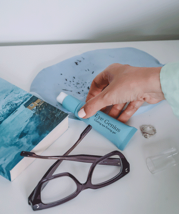 Pem Delian Eye Genius hűsítő szemkörnyékfeszesítő gél kupak nélkül kézben, szemüveg, könyv, gyűrű mellett