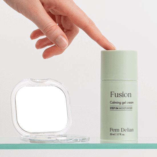 Pem Delian Fusion bőrnyugtató gélkrém üveg polcon, rámutat a tetejére a modell, mellette egy kis kozmetikai tükör