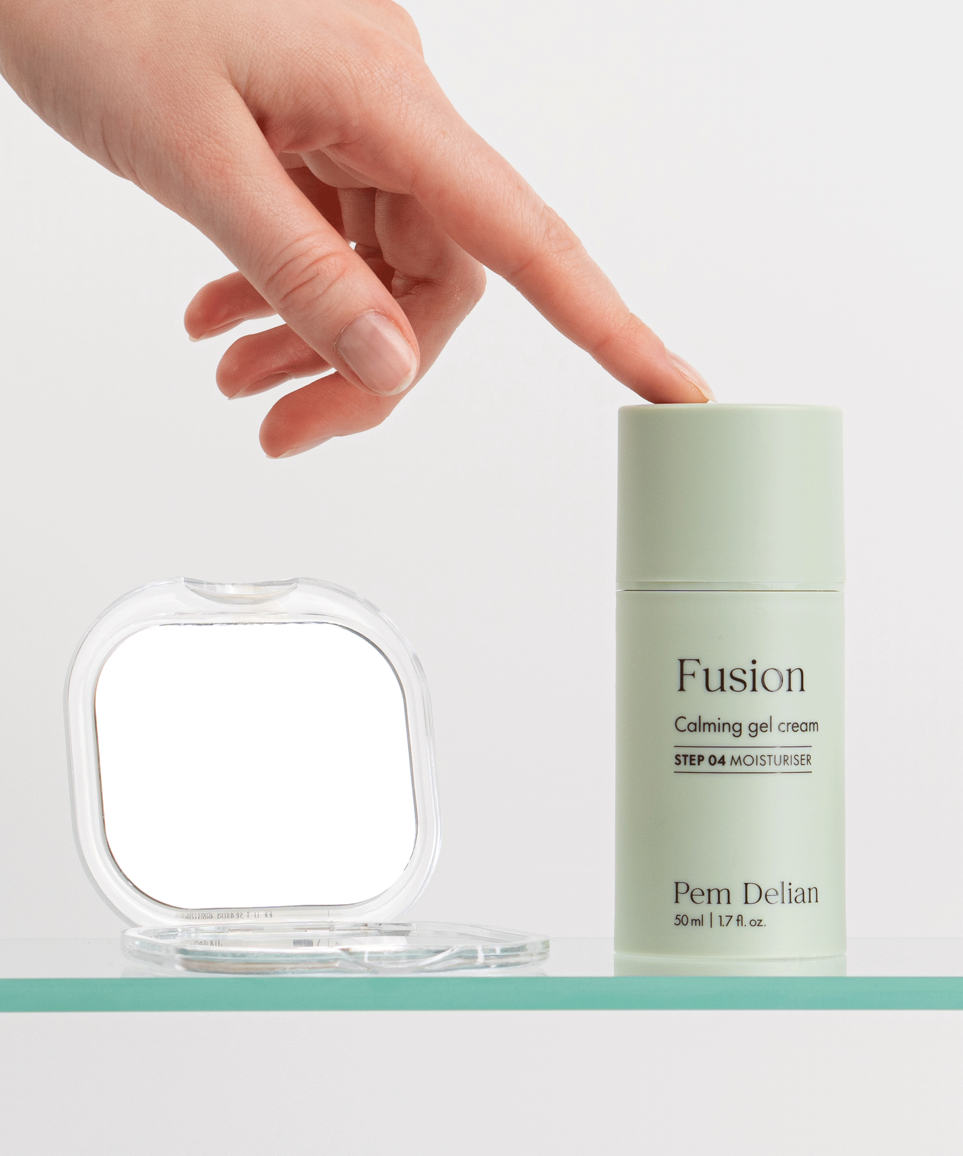 Pem Delian Fusion bőrnyugtató gélkrém üveg polcon, rámutat a tetejére a modell, mellette egy kis kozmetikai tükör