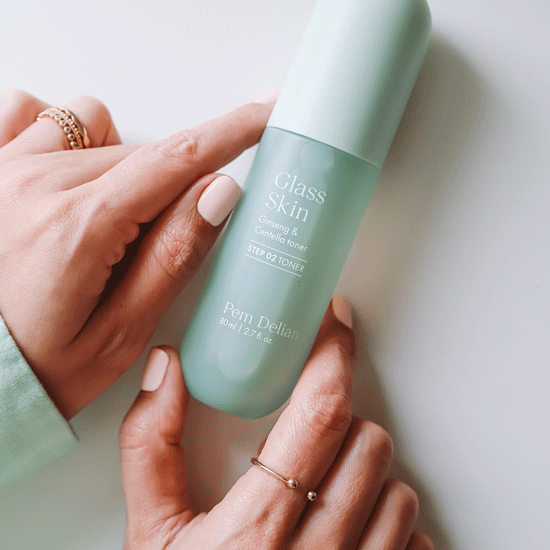 Pem Delian Glass Skin Ginseng & Centella toner asztalon, modell a kezével tartja, a kézen ékszerek