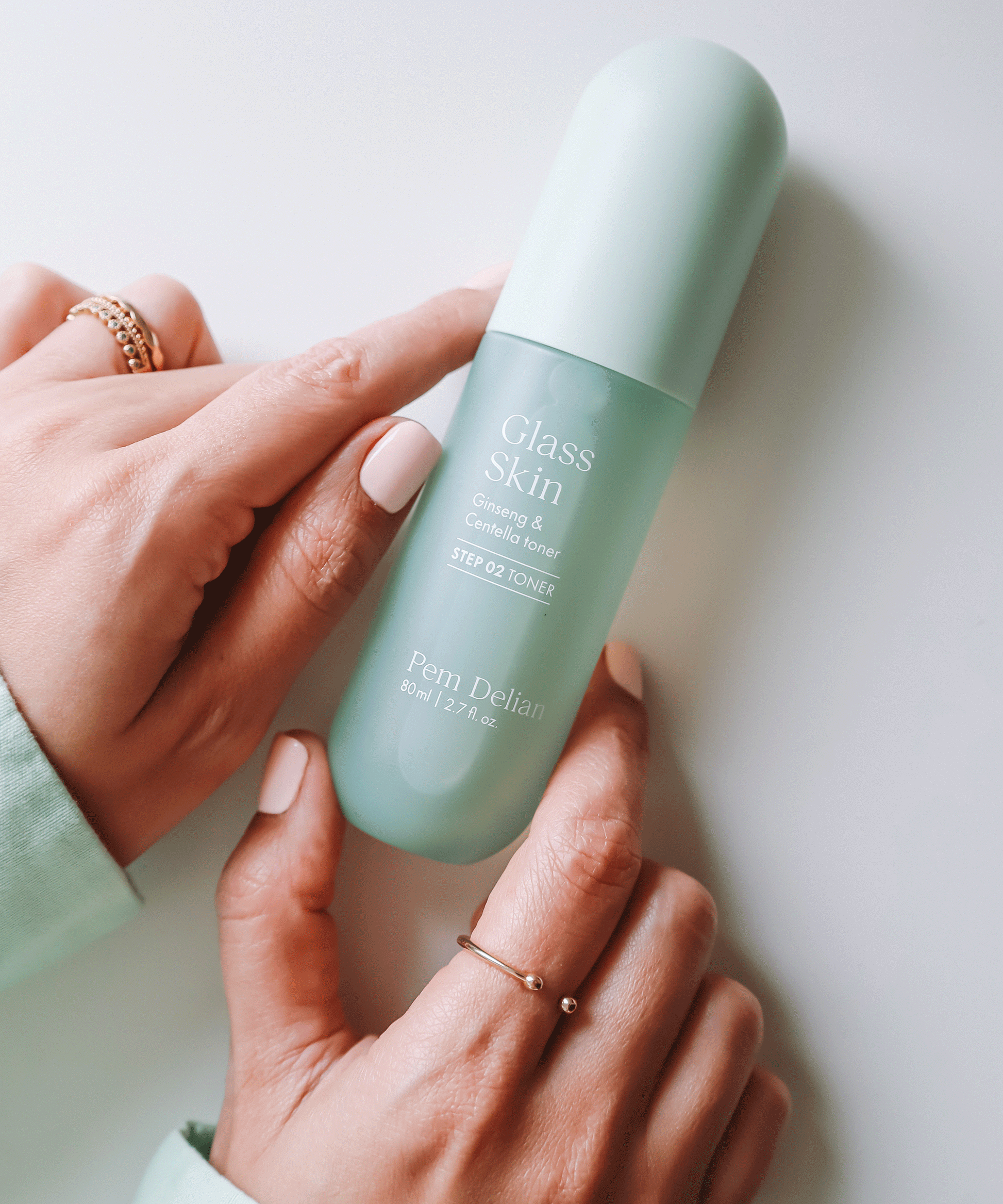 Pem Delian Glass Skin Ginseng & Centella toner asztalon, modell a kezével tartja, a kézen ékszerek