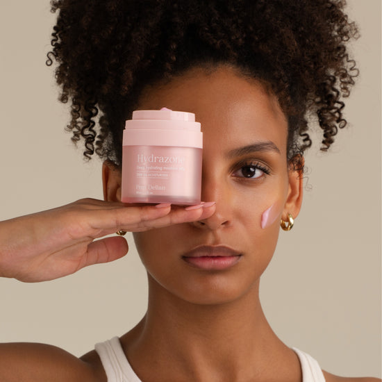 Pem Delian Hydrazone rózsaszínű arcápoló zselé tégely a modell kezén, textúra az arcon 