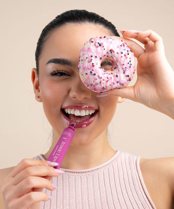 Pem Delian Iconic Lips Berry bogyós gyümölcs ízű ajakápoló mosolygó modell kezében, fánkkal a szem előtt