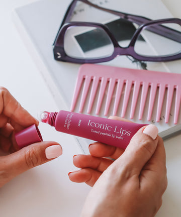 Iconic Lips Berry színezett peptides ajakápoló tubus és applikátor szemüveg és rózsaszín fésű előtt