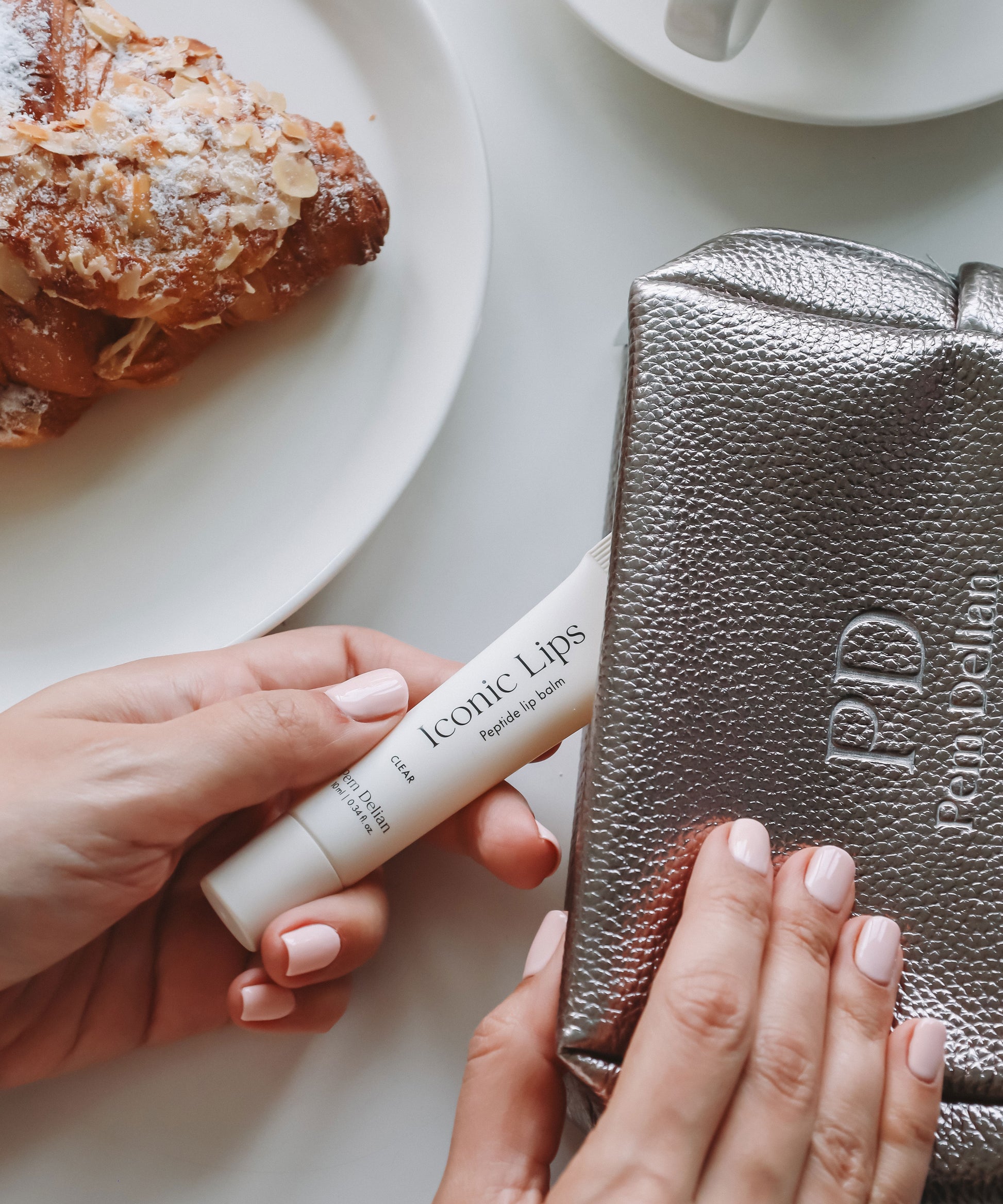 Pem Delian Iconic Lips clear peptides ajakápolót neszeszerből kiveszik, mellette tányéron péksütemény