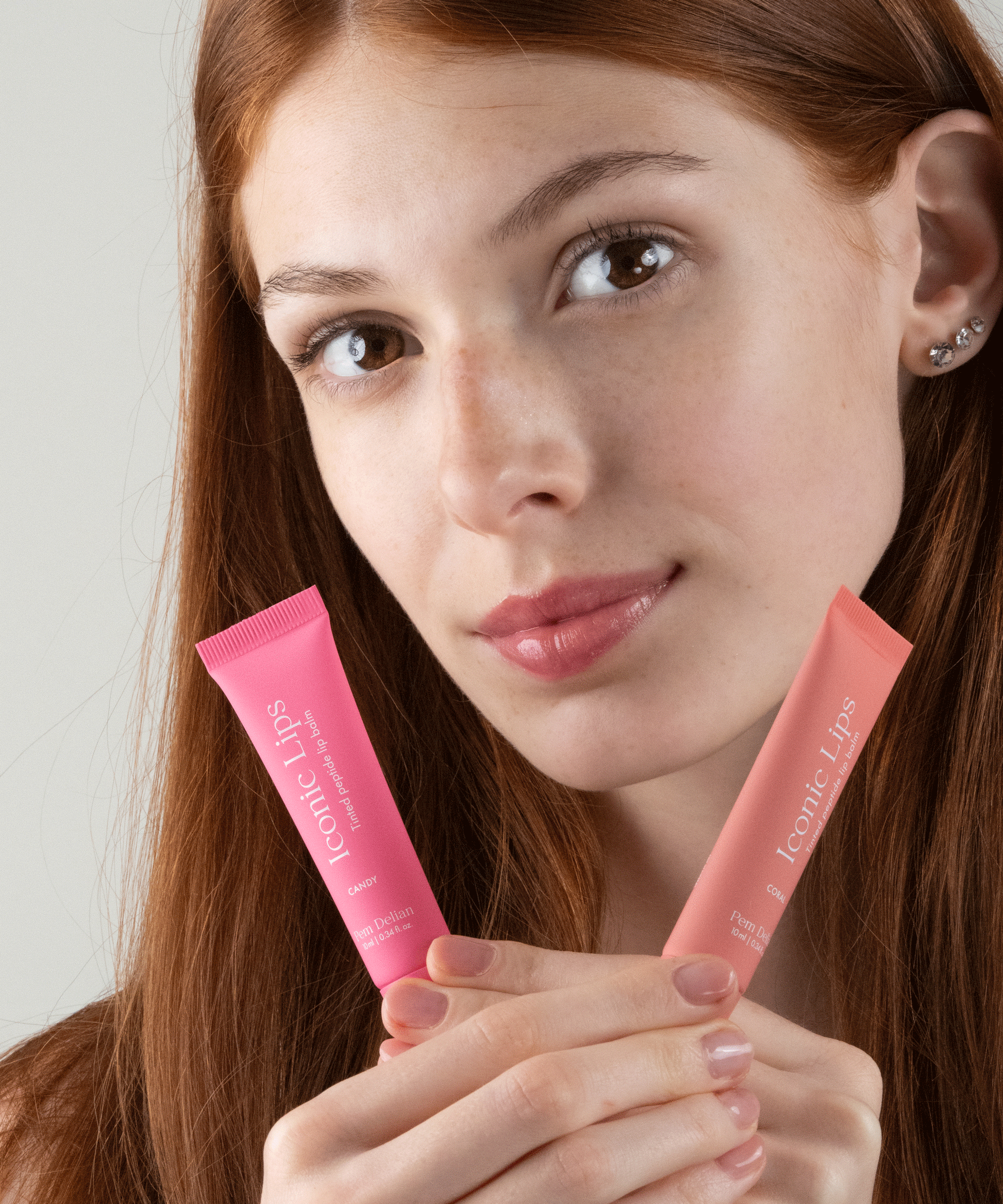 Pem Delian Iconic Lips coral és candy színezett, peptides ajakápoló vörös hajú modell kezében