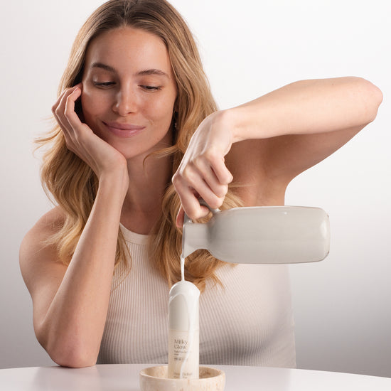 Pem Delian Milky Glow toner tejjel leöntve egy kancsóból a mosolygó modell által, fehér háttérrel