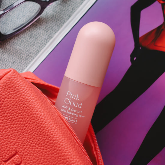 Pem Delian Pink Cloud NMF & Glycoin Ultra hidratáló toner korall színű kozmetikai táskában, mellette egy szemüveg és magazin