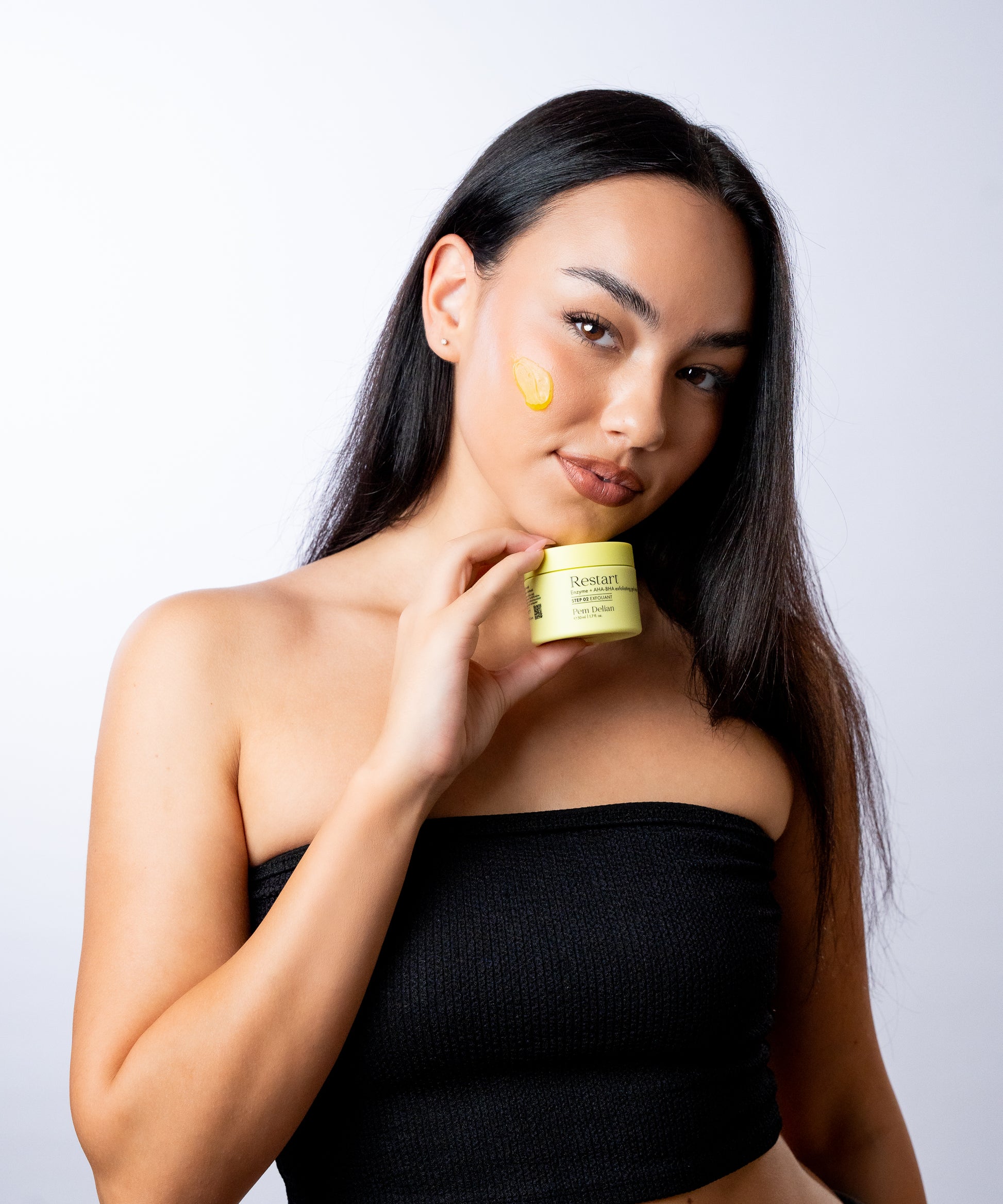Pem Delian Restart Enzim + AHA-BHA hámlasztó gélmaszk barna hajú modell álla alatt tartva, a géles sárga textúra az arcára kikenve