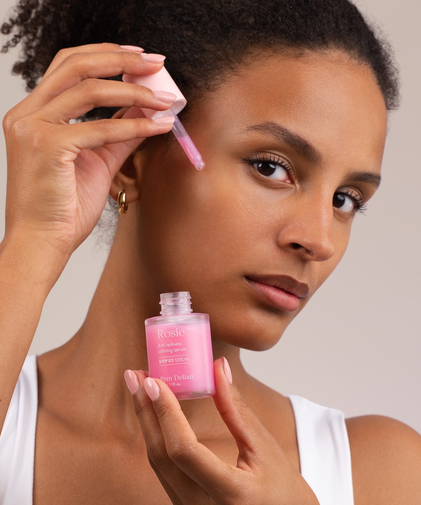 Pem Delian Rosie bőrpír elleni nyugtató szérum pipettája a modell arca előtt, tégely a kézben