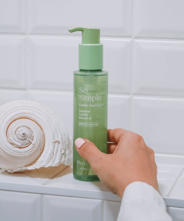 A Pem Delian So Simple olajos arctisztítót a modell a fürdőszoba polcára teszi, bal oldalt egy csiga alakú kagylóval