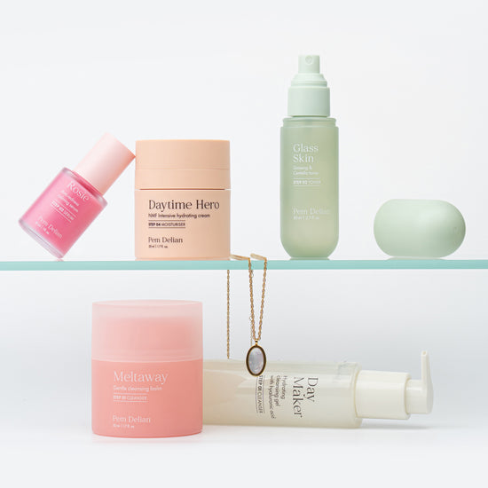 Pem Delian Rosie szérum, Daytime Hero hidratáló, Glass Skin arcpermet, Meltaway balzsam és Day Maker lemosó üvegpolcon elhelyezve nyaklánc mellett