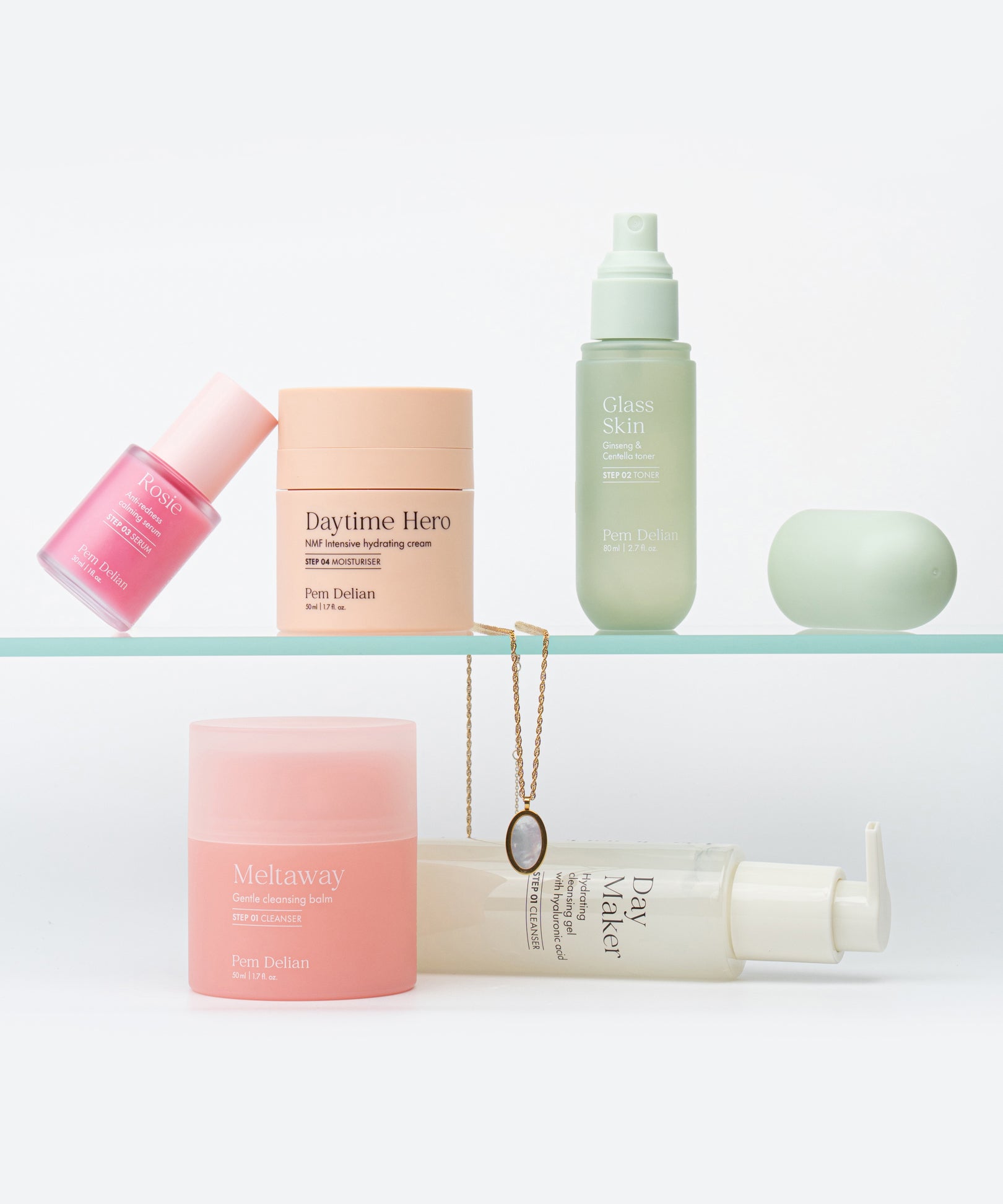 Pem Delian Rosie szérum, Daytime Hero hidratáló, Glass Skin arcpermet, Meltaway balzsam és Day Maker lemosó üvegpolcon elhelyezve nyaklánc mellett